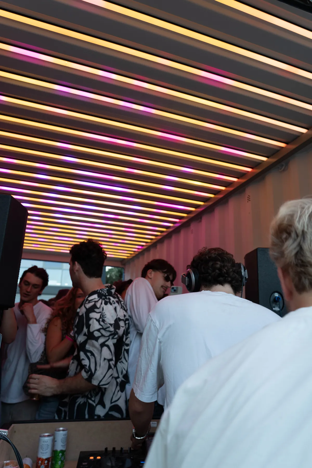 DJ achter de booth in de RAVEBOX feestcontainer met roze en gele lichtshow en dansende bezoekers