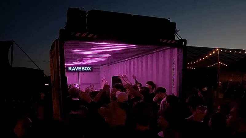 RAVEBOX container met roze lichtshow en feestend publiek bij schemer op Classified Outdoor: Off The Grid